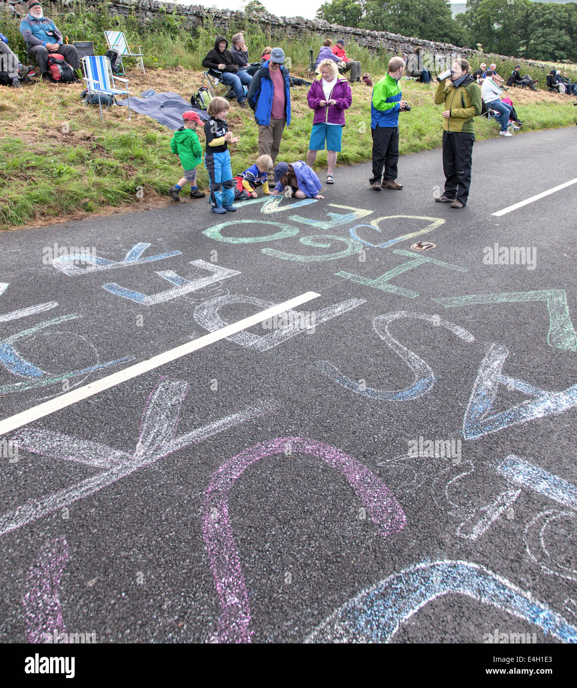 Children chalking riders names on the road before the arrival of the Tour De France near Hawes, North Yorkshire, England, UK Stock Photo