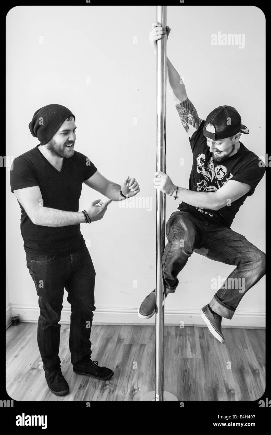 Two young men playing on a sports pole, learning how to pole dance Stock Photo