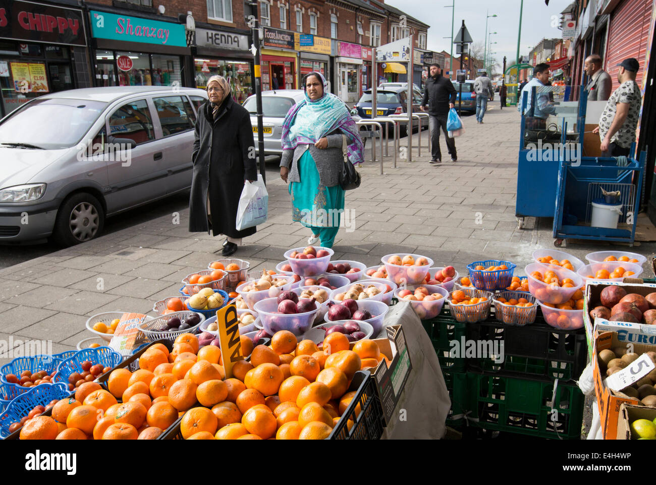 Two Muslim women walk past a greengrocer in the centre of the mainly Asian area of Lozells in Birmingham, UK Stock Photo