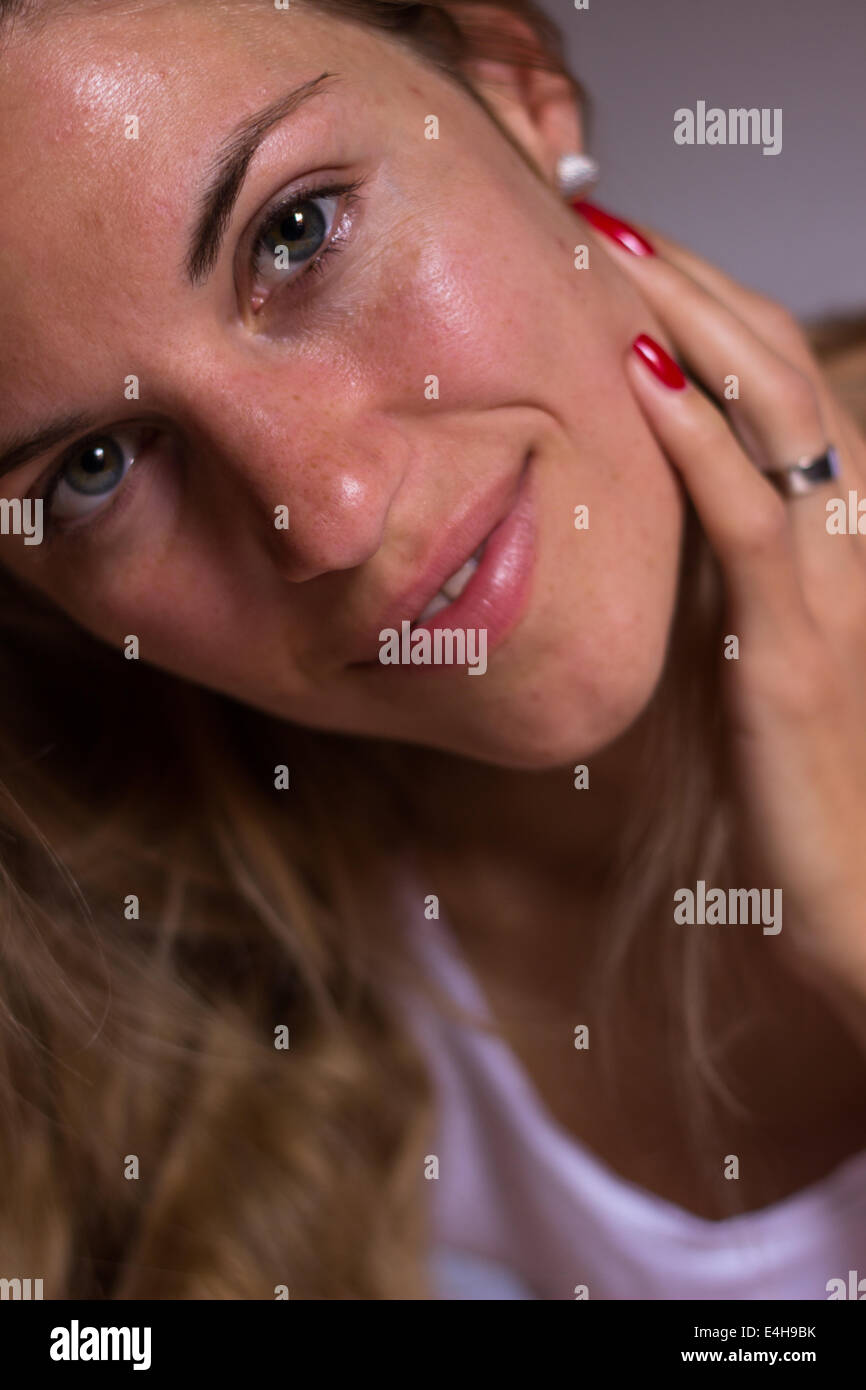 young beautiful woman face closeup portrait 'touching face' indoors smiling 'looking at camera' Stock Photo