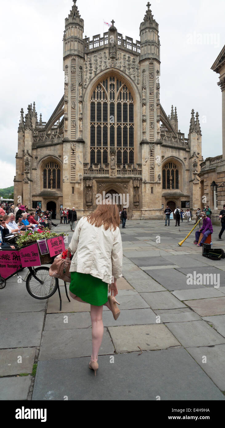 A woman with tired feet  in high heels standing on one leg checks her shoe outside Bath Abbey in Bath Spa, Somerset and Avon England UK   KATHY DEWITT Stock Photo