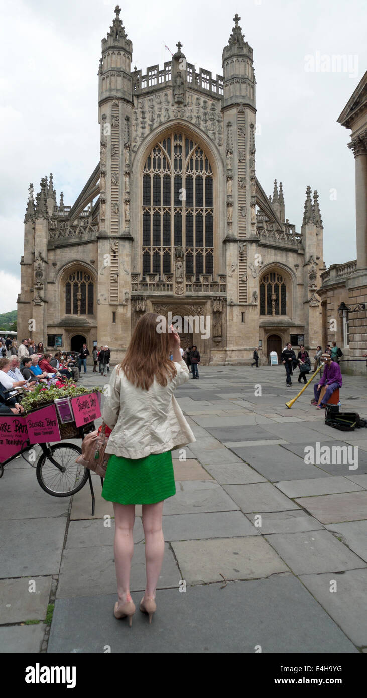 A woman tourist in green skirt and high heels standing photographing the building outside Bath Abbey in Bath Spa, Somerset an England UK  KATHY DEWITT Stock Photo