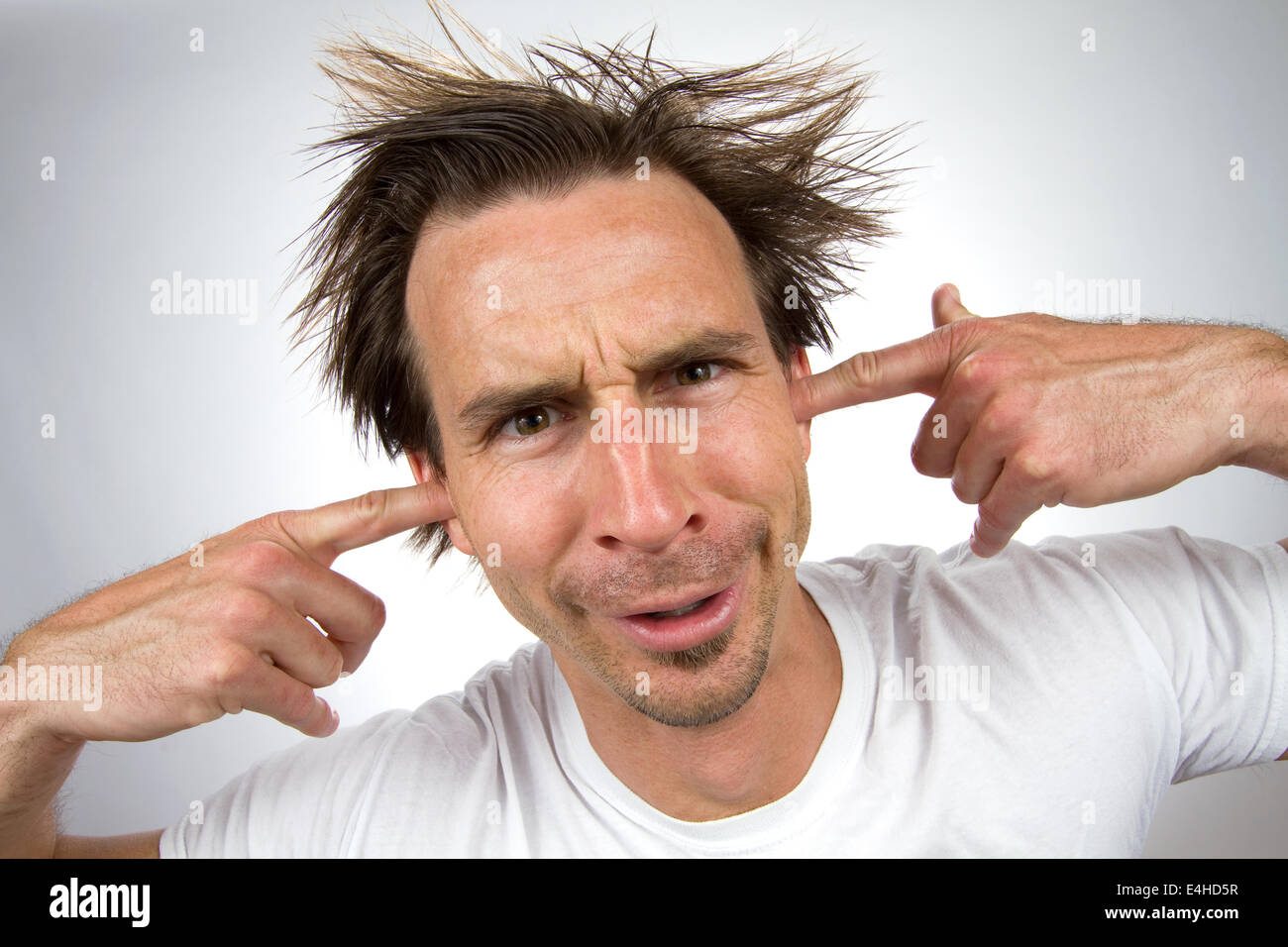 Scruffy unpleasant looking man with a silly facial expression and unruly hair puts his fingers in his ears so that he can not he Stock Photo