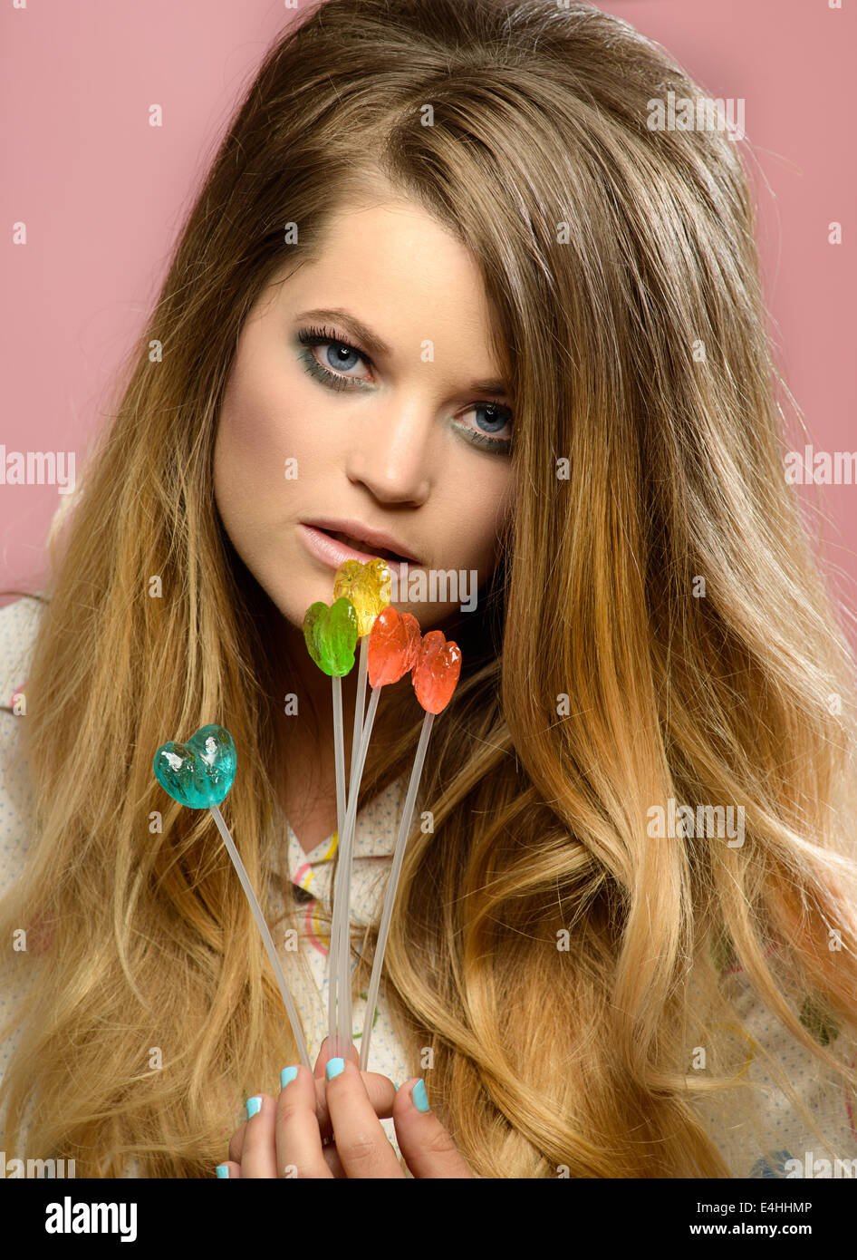 A pretty blond woman holding colorful heart candies, tilting her head posing. She has a 60s big hairstyle looking romantic. Stock Photo