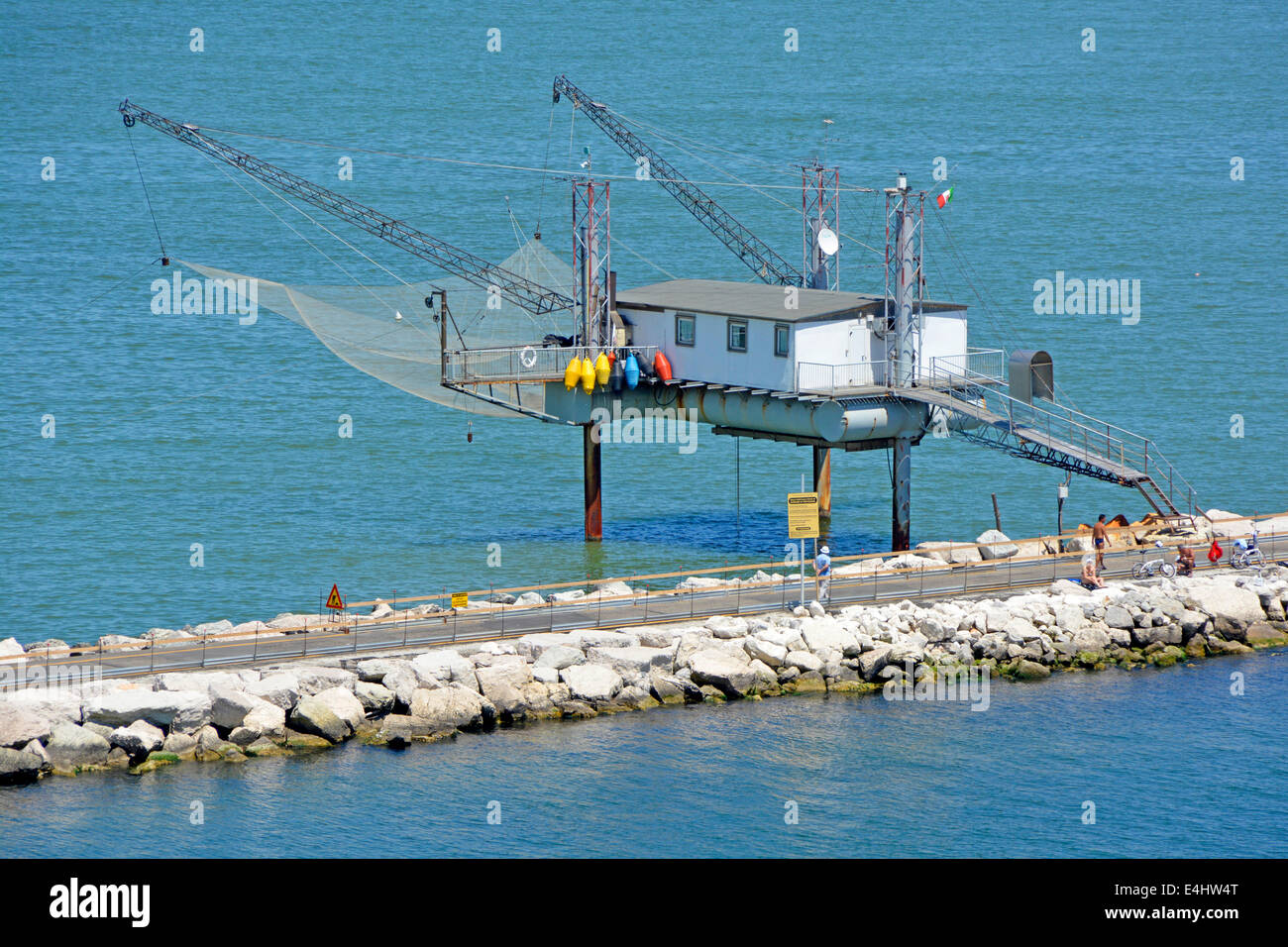 Closeup of unusual fishermens hut on stilts with large suspended net & access from public path along harbour breakwater Stock Photo