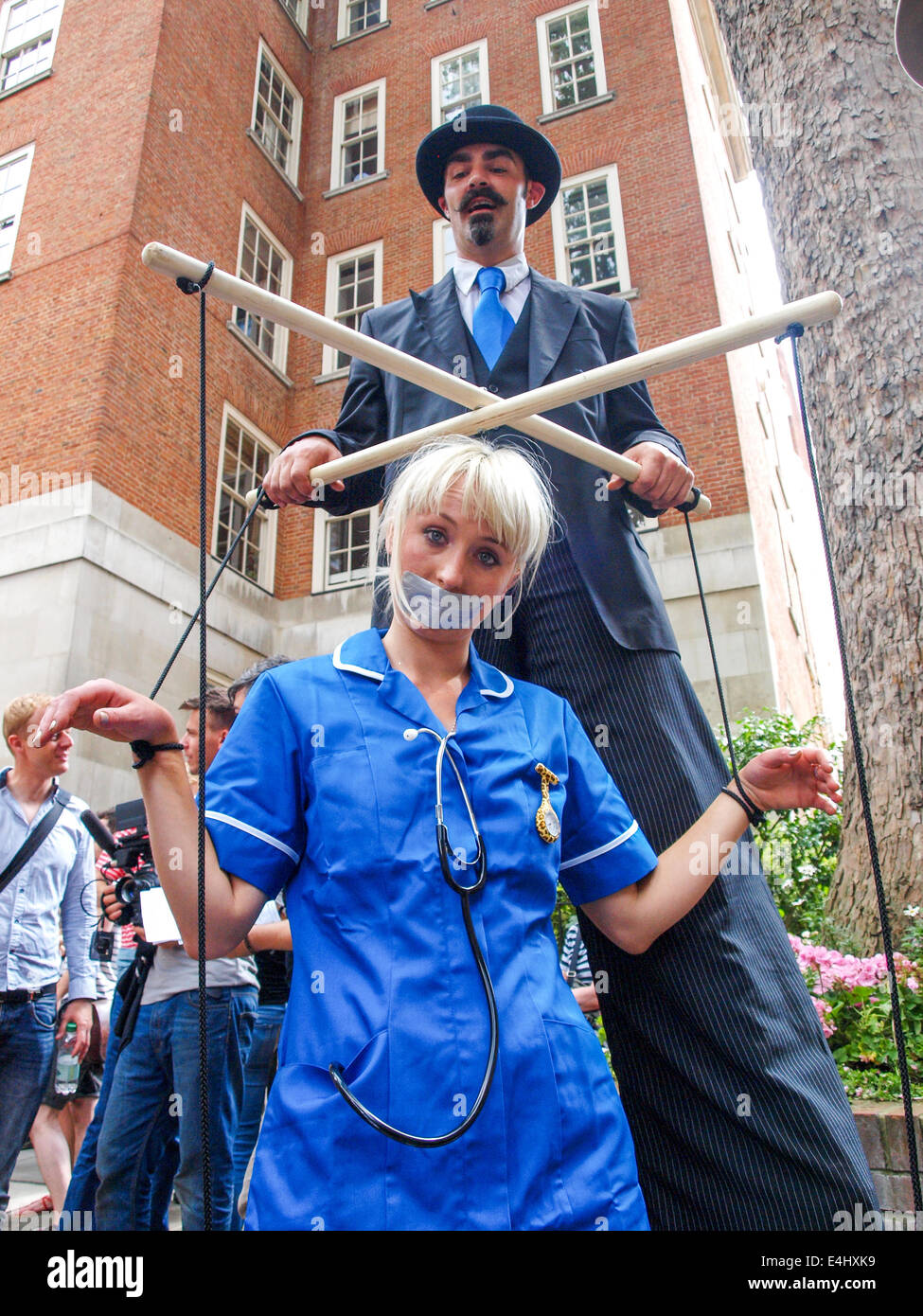 London, UK. 12th July, 2014.  A puppet master on stilts pulls the strings of a human NHS nurse who is gagged with tape, during the anti-Transatlantic Trade and Investment Partnership (TTIP) protest in Smith Square. Credit:  Mamusu Kallon/Alamy Live News Stock Photo