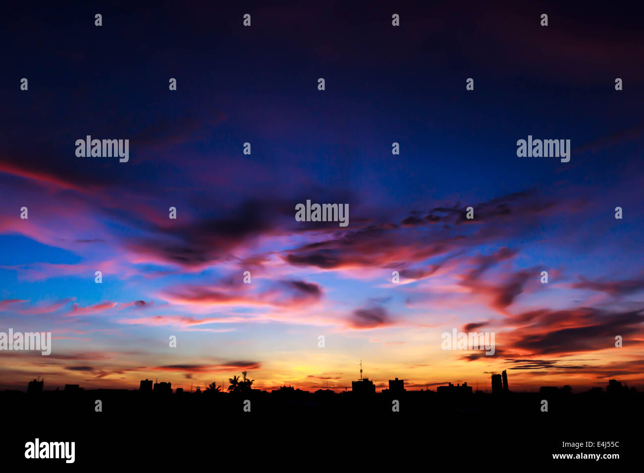 The sun sets behind a silhouetted city. Stock Photo