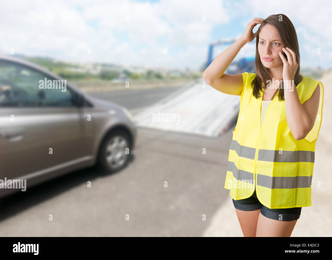 Woman talking on the phone wearing a reflector vest near her broken car Stock Photo