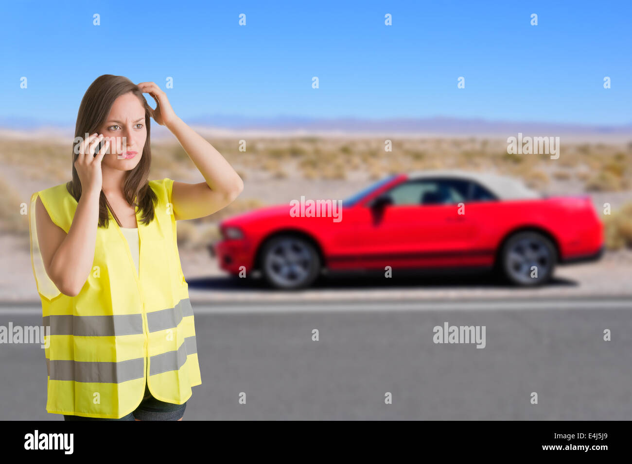 Woman talking on the phone wearing a reflector vest next to her broken car Stock Photo