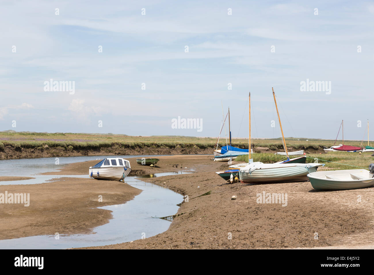 Boats beached with the tide out in a muddy tidal creek in the harbour in Blakeney, a north Norfolk coastal village, UK Stock Photo