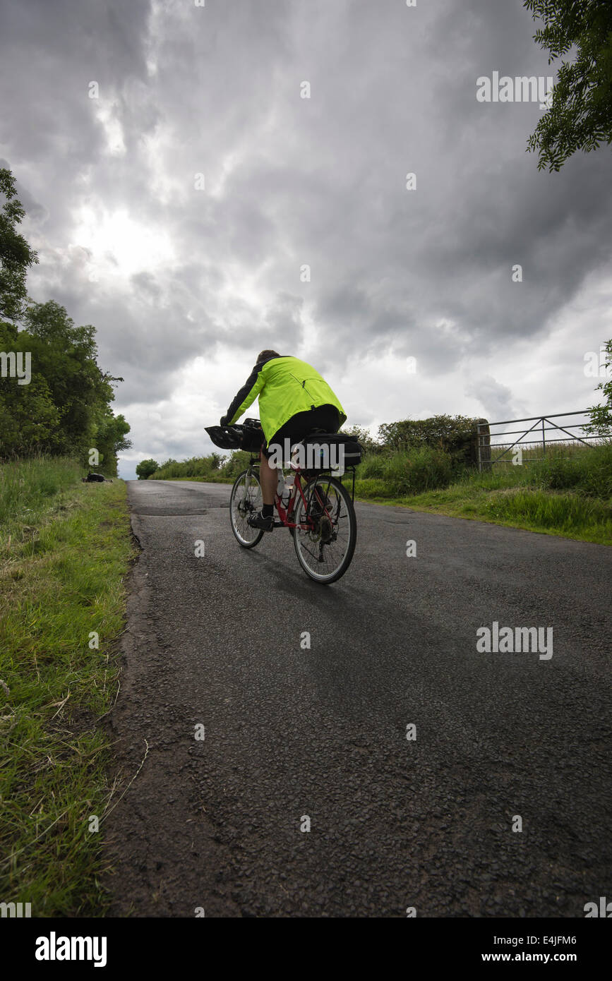 Cyclist cycling up a hill between Haltwhistle and Twice Brewed in Northumberland under a heavy sky. Stock Photo