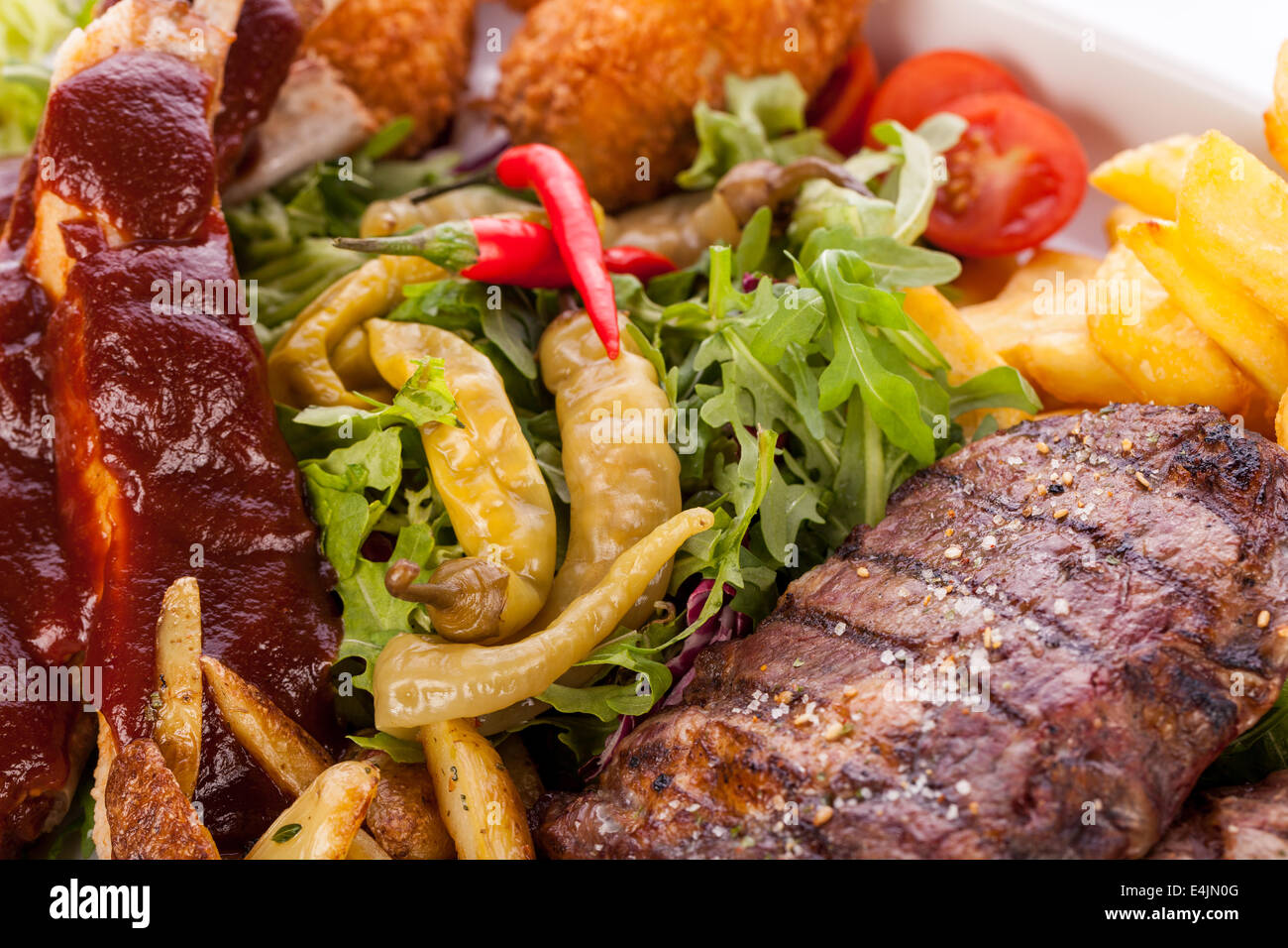 Wholesome platter of mixed meats including grilled steak, crispy crumbed chicken and beef on a bed of fresh leafy green mixed salad served with French fries and chutney or BBQ sauce in a dish Stock Photo