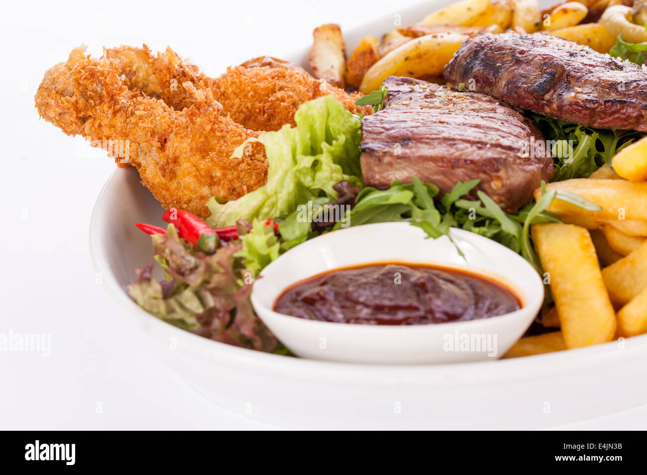 Wholesome platter of mixed meats including grilled steak, crispy crumbed chicken and beef on a bed of fresh leafy green mixed sa Stock Photo
