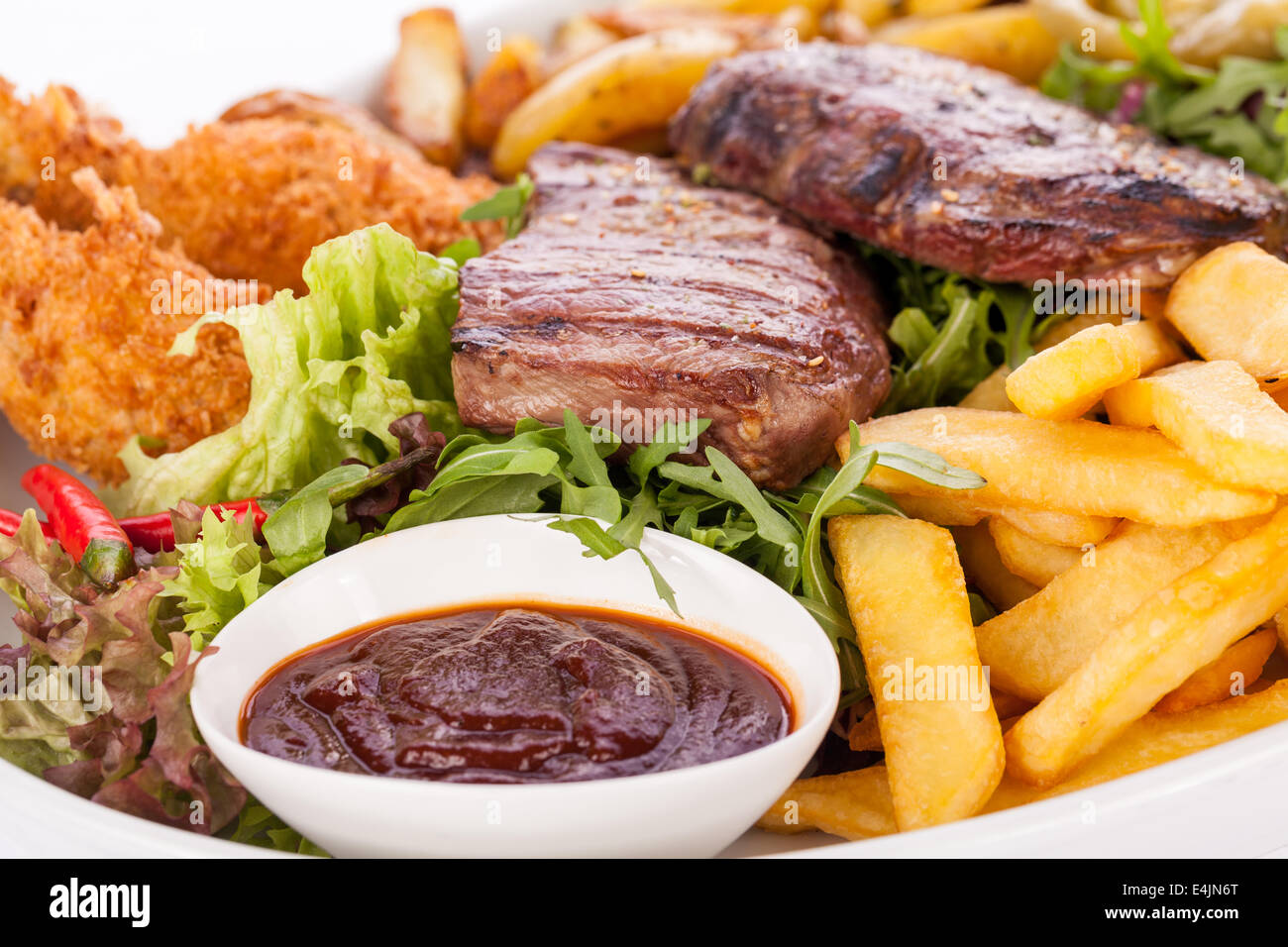 Wholesome platter of mixed meats including grilled steak, crispy crumbed chicken and beef on a bed of fresh leafy green mixed salad served with French fries and chutney or BBQ sauce in a dish Stock Photo