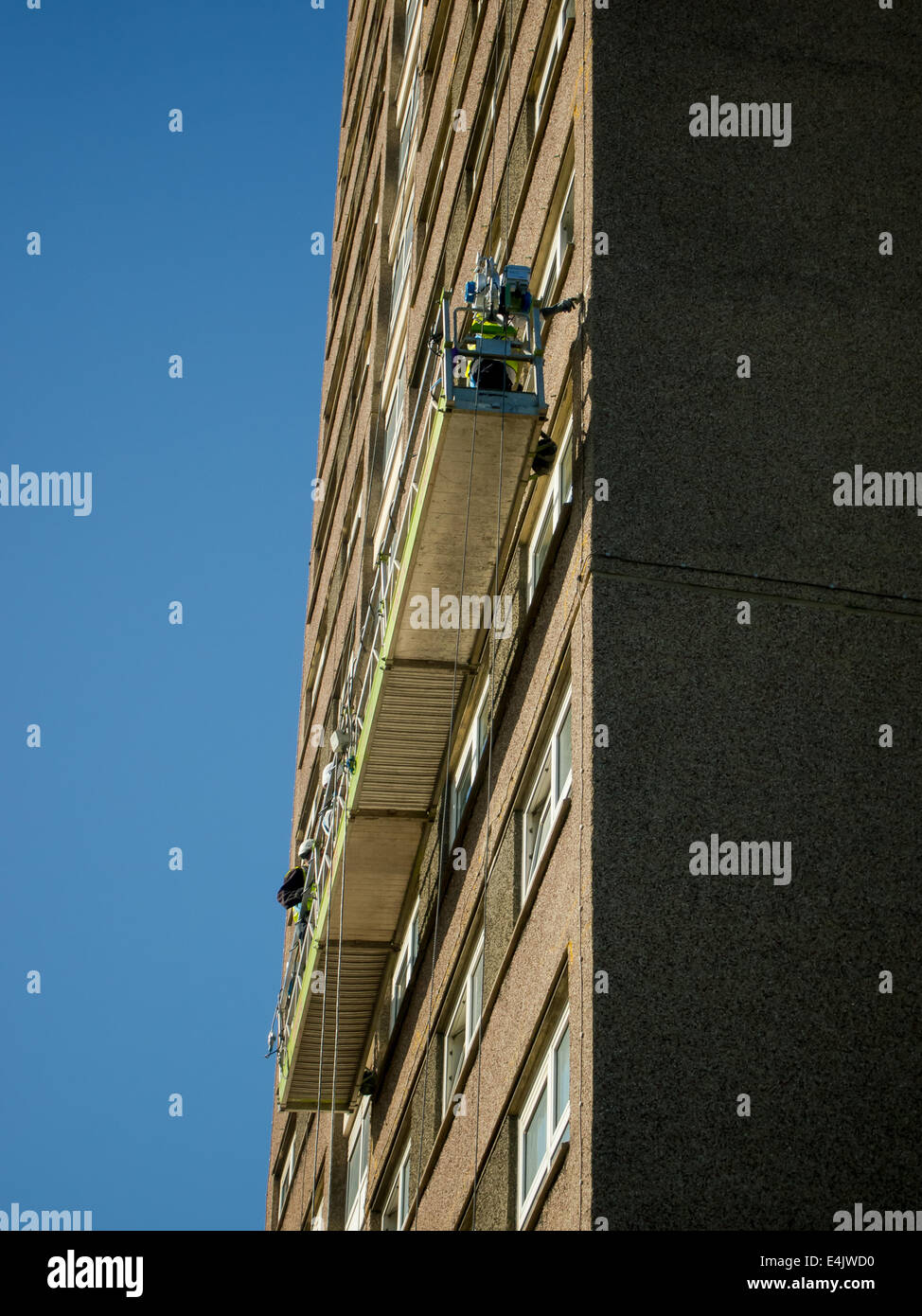 Workmen in a suspended platform carry out concrete repairs on a high rise tower block Stock Photo