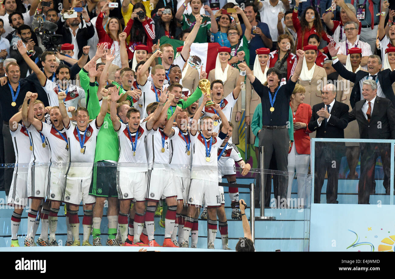 Philipp Lahm (2-R) of Germany lifts up the World Cup trophy with his teammates Lukas Podolski (3-R) and Thomas Mueller (R) and head coach Joachim Loew (2nd row 4-R), German Chancellor Angela Merkel (2nd row 3-R), FIFA President Joseph Blatter (2nd row 2-R) German President Joachim Gauck (2nd row R), president of the German Football Association (DFB), Wolfgang Niersbach (3rd row R), and assistant coach Hansi Flick (2nd row L) and team manager Oliver Bierhoff (2nd row 2-L) after winning the FIFA World Cup 2014 final soccer match between Germany and Argentina at the Estadio do Maracana in Rio de Stock Photo