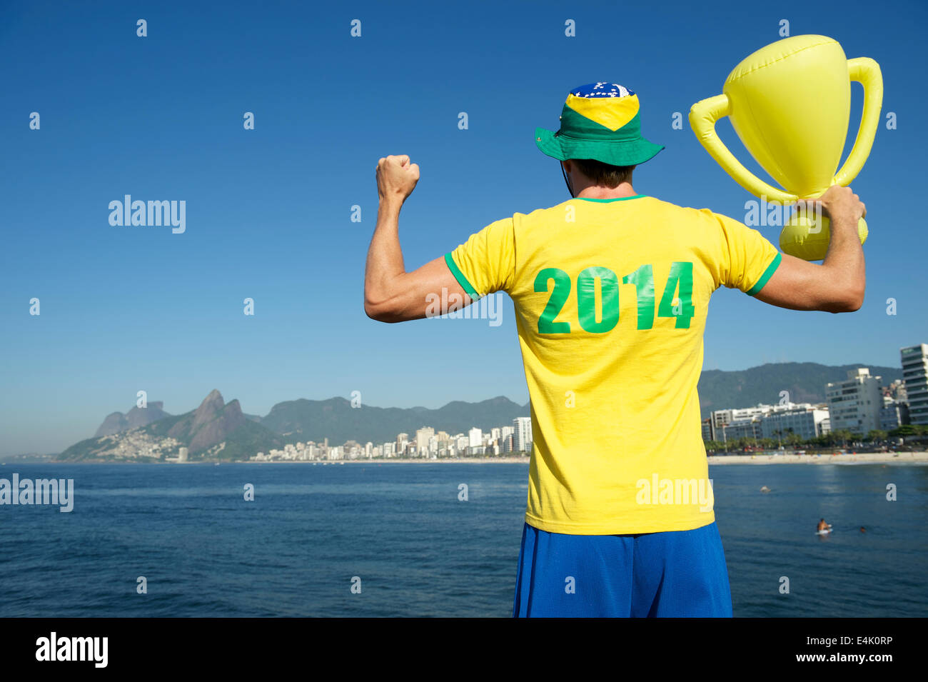 Brazilian man in 2014 shirt in Brazilian colors celebrating with trophy in front of sea view Ipanema Beach Rio de Janeiro Stock Photo