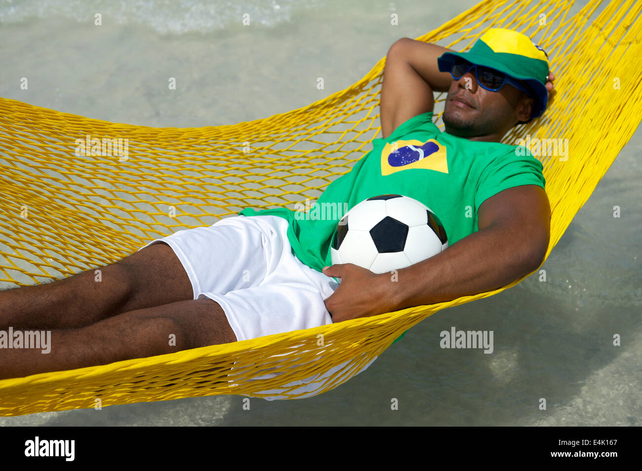 Brazilian football player wearing Brazilian flag hat relaxing in beach hammock with a soccer ball Stock Photo