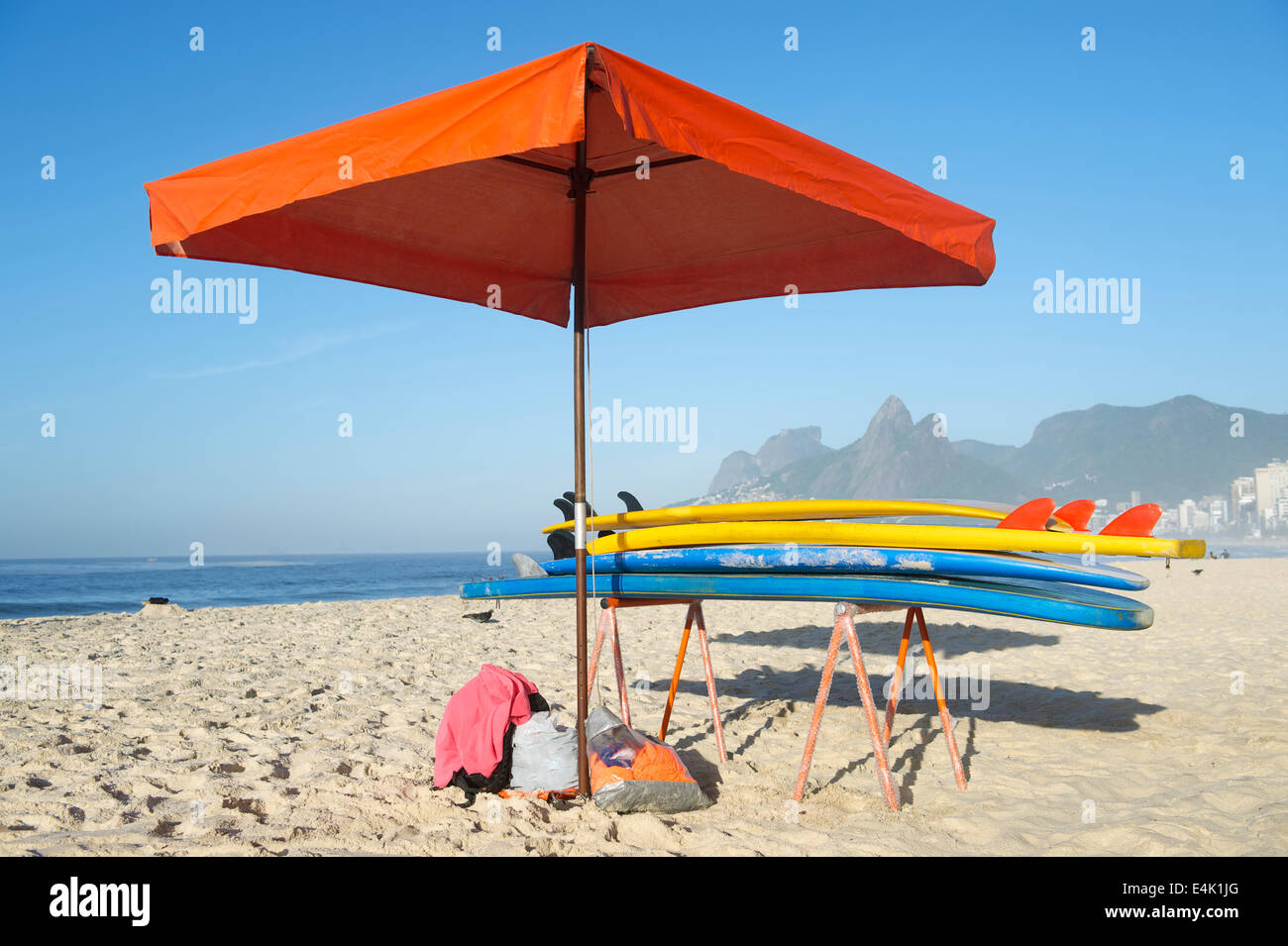 Colorful stand up paddle long board surfboards stacked next to beach umbrella on Ipanema Beach Rio de Janeiro Stock Photo