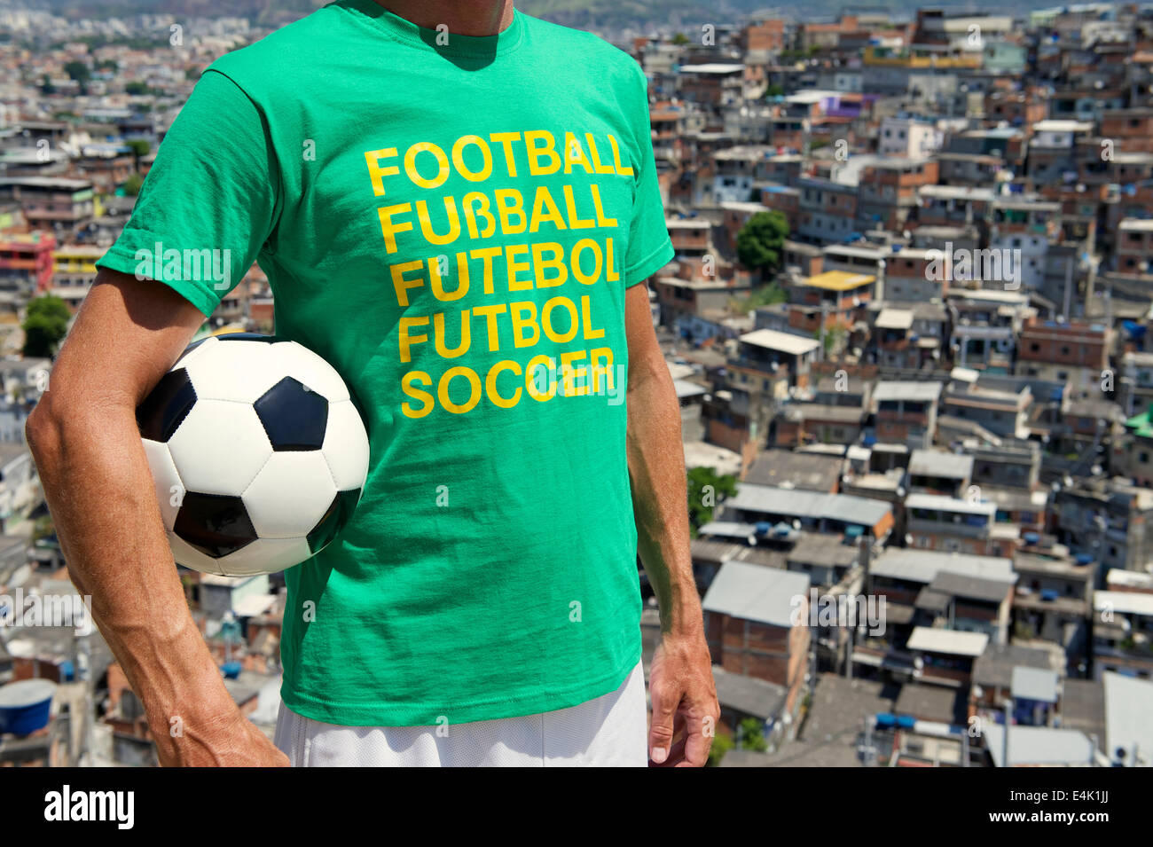 Brazilian man standing in international football t-shirt holding soccer ball in front of favela slum background Rio de Janeiro Stock Photo