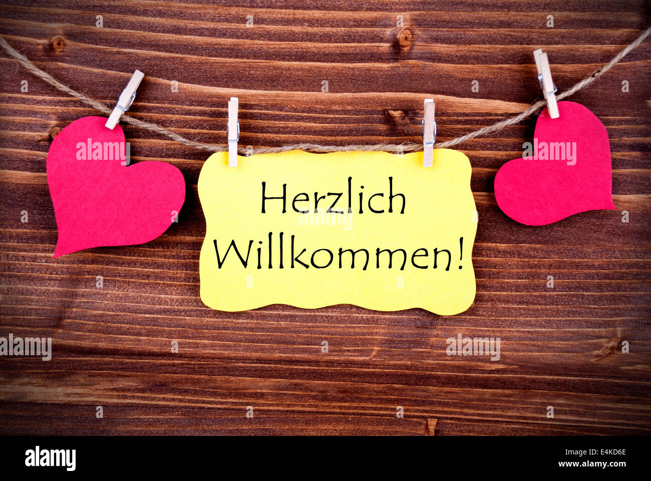 Yellow Label with the German Words Herzlich Willkommen which means Welcome, Hanging on a Line with Hearts Stock Photo