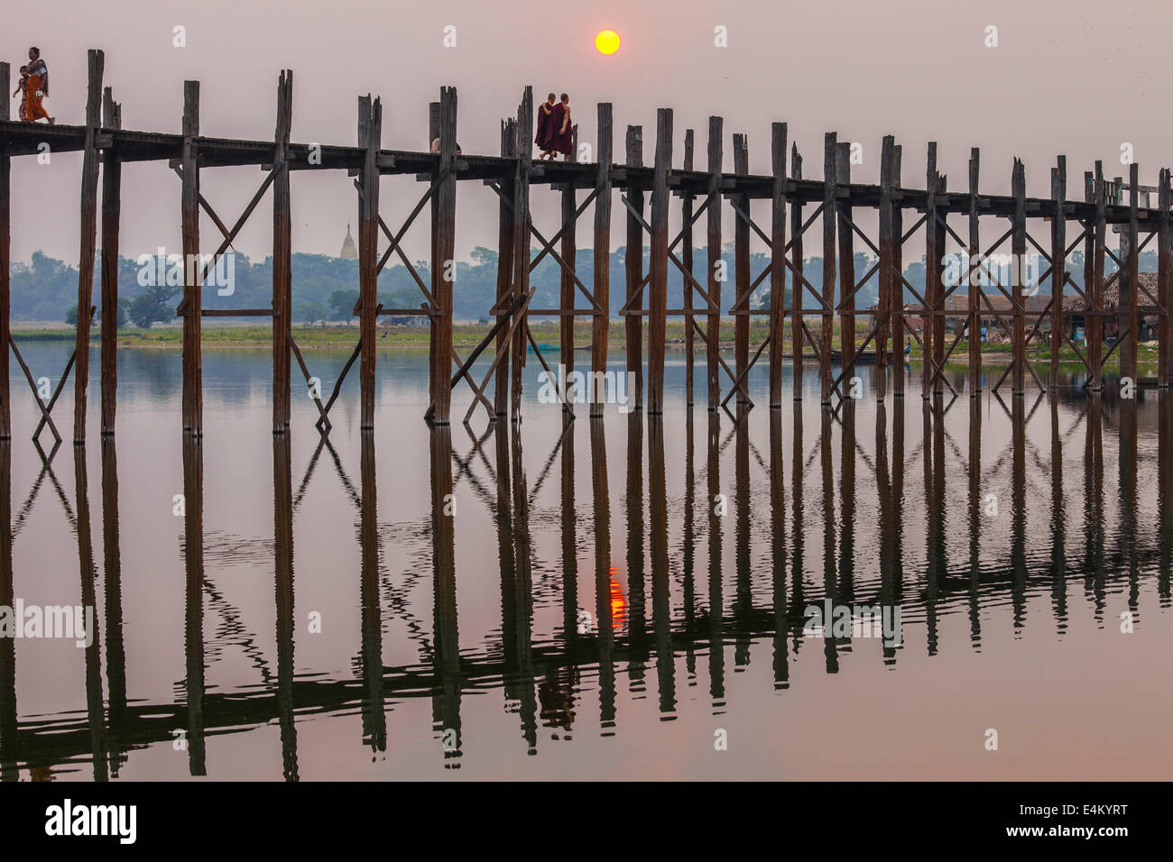 Monks stroll across the U Bein Teak Bridge at sunset. The bridge spans ...