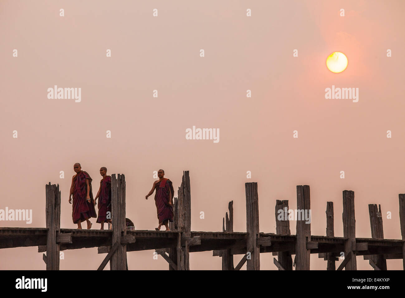 Monks stroll across the U Bein Teak Bridge at sunset. The bridge spans ...