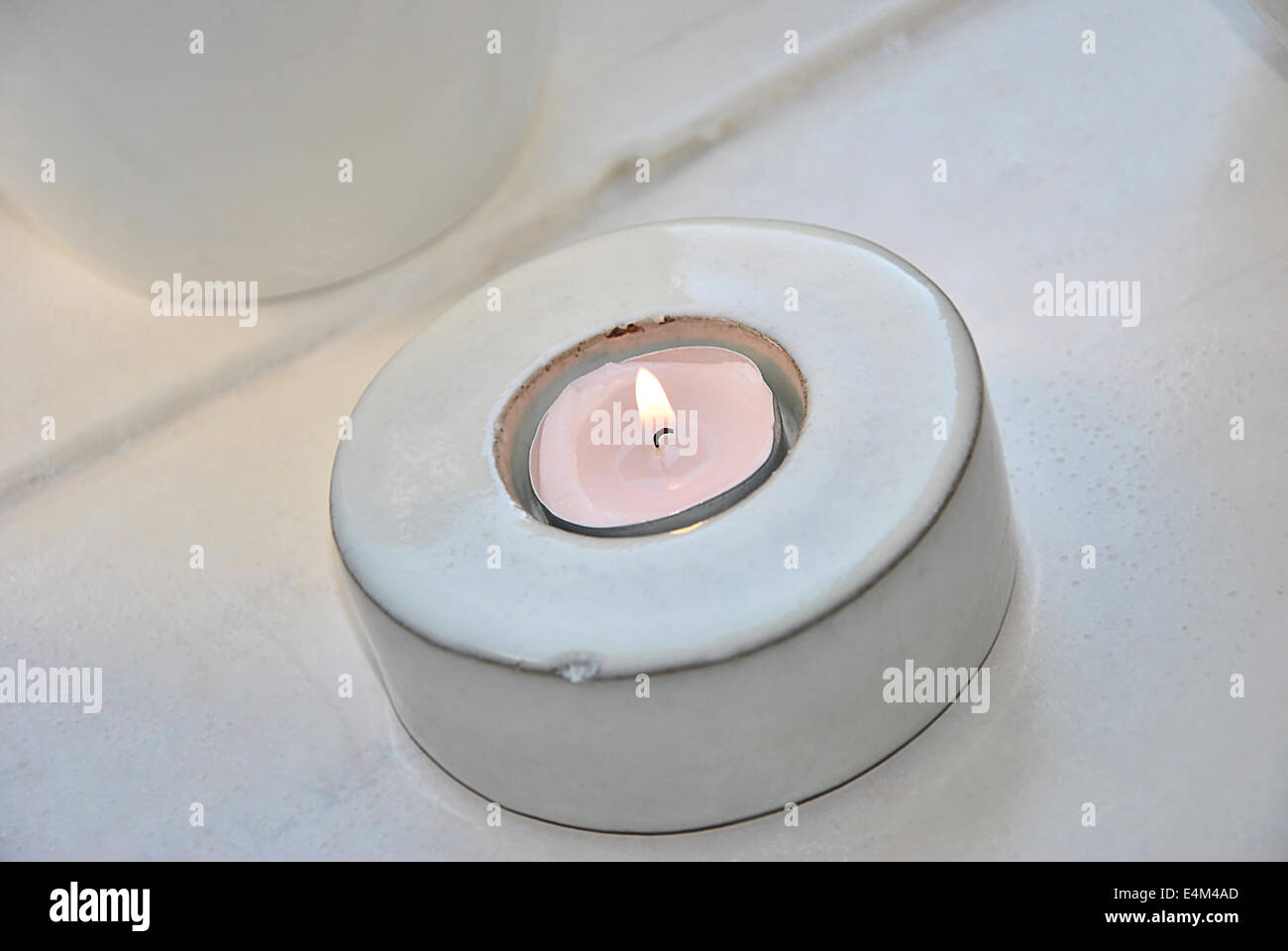 burning tea light in a white candlestick holder, close up, on white background Stock Photo