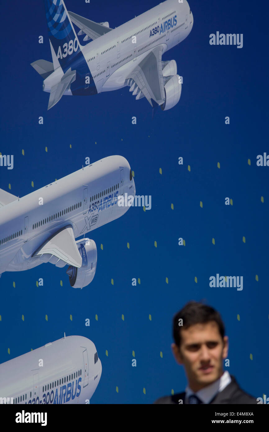 A visitor beneath a billboard of examples of the Airbus airliner fleet on the side of the Airbus corporate chalet at the Farnborough Air Show, England. Airbus is an aircraft manufacturing division of Airbus Group (formerly European Aeronautic Defence and Space Company). Based in Blagnac, France, a suburb of Toulouse, with production and manufacturing facilities mainly in France, Germany, Spain and the United Kingdom, the company produced 626 airliners in 2013. Stock Photo