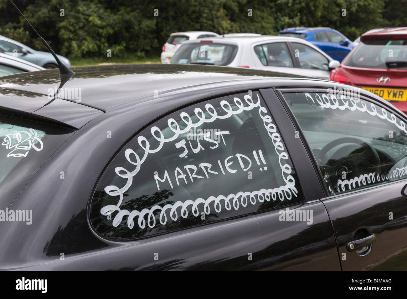 Window of honeymooners' black car painted with 'Just Married!!' Stock Photo