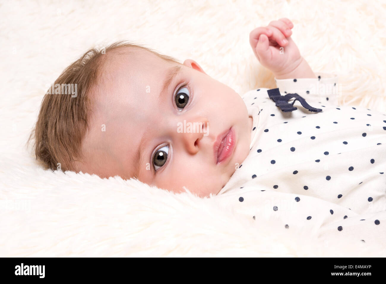 Portrait of Beautiful Baby Girl in Spotty Top resting on Cream Fur Rug Stock Photo