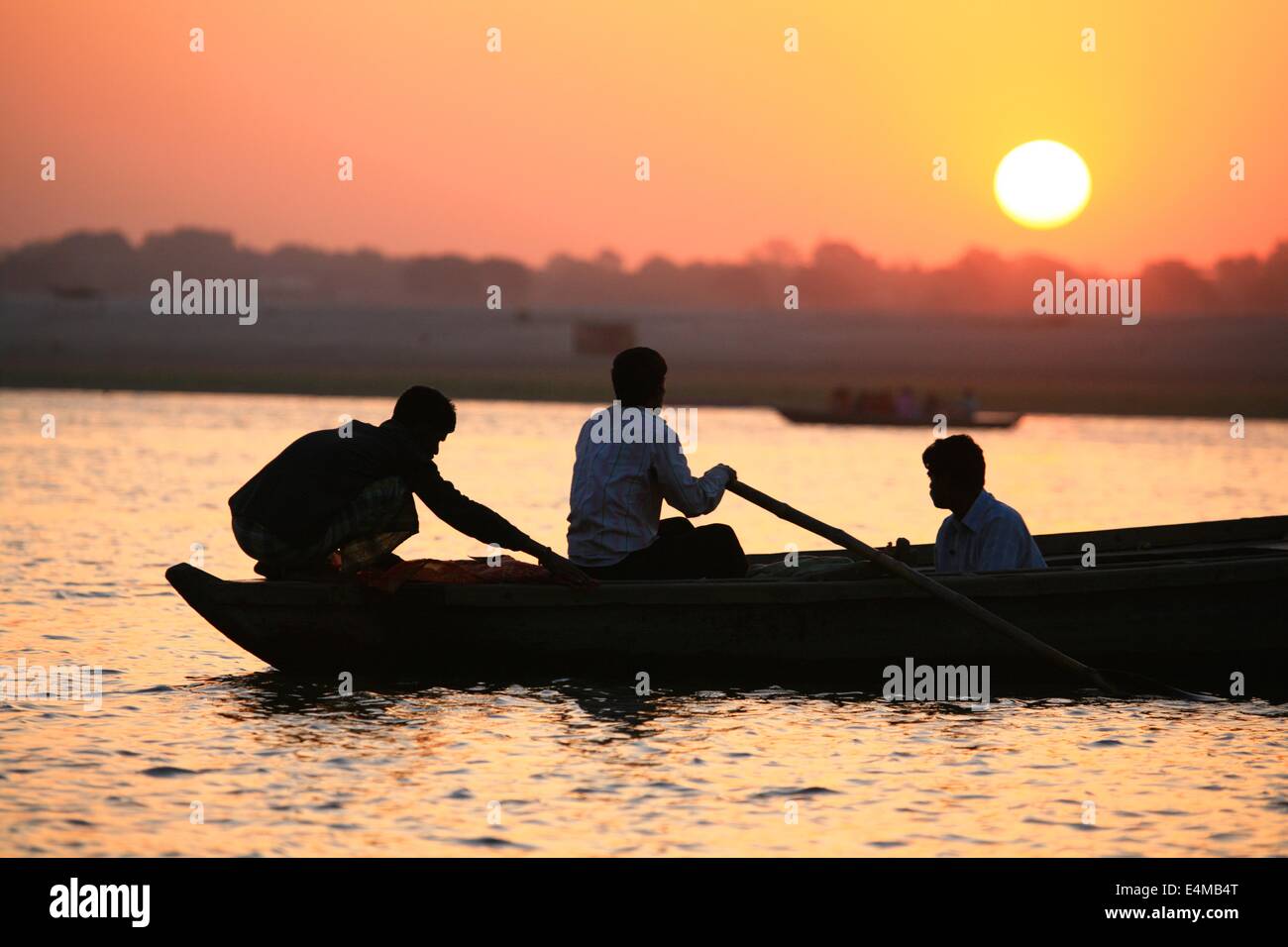 Sun sets over the Ganges silhouetting a boat with three people in it. Stock Photo