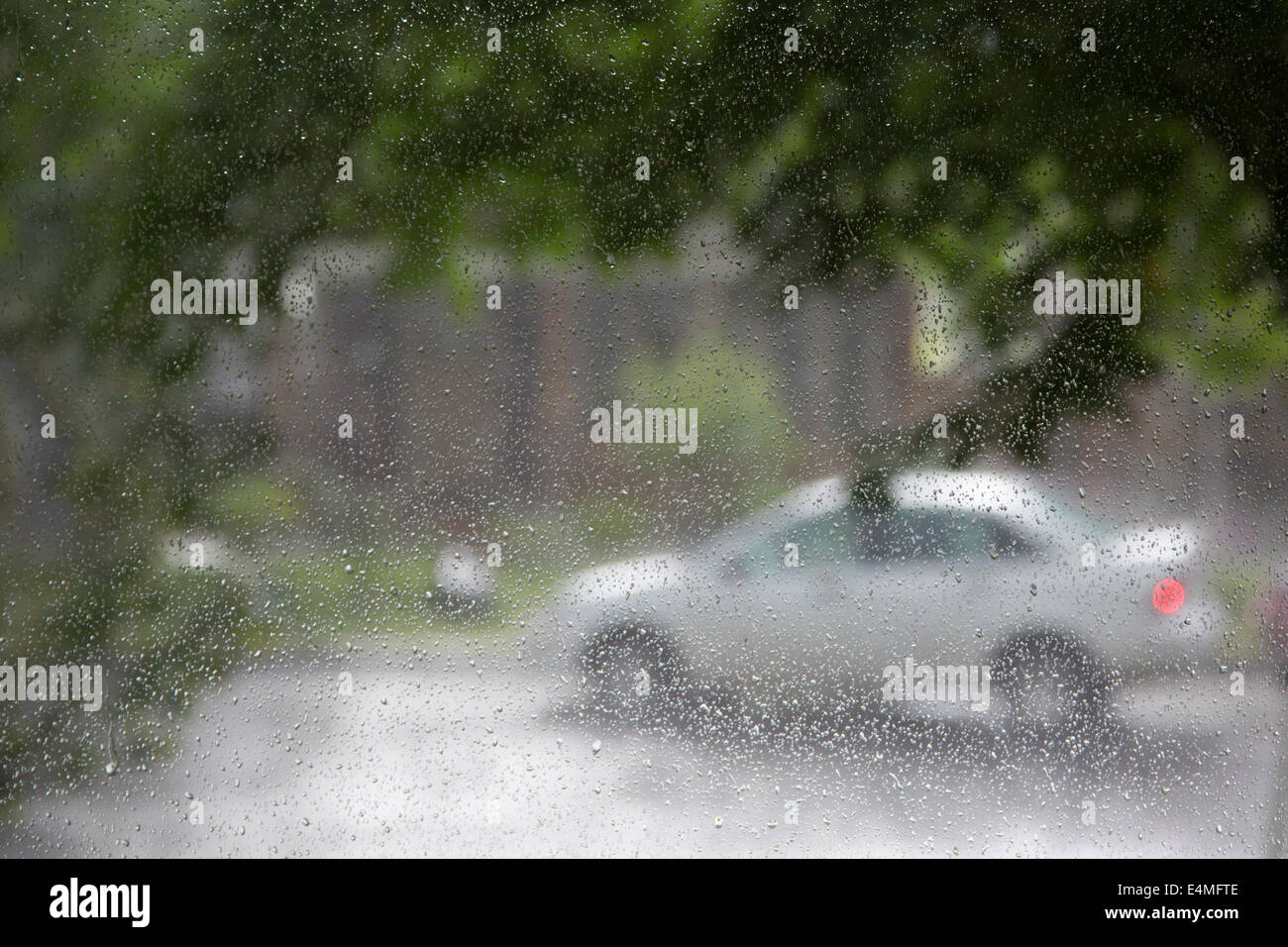 Car on city street during a rainy day seen through raindrops on window of house Stock Photo