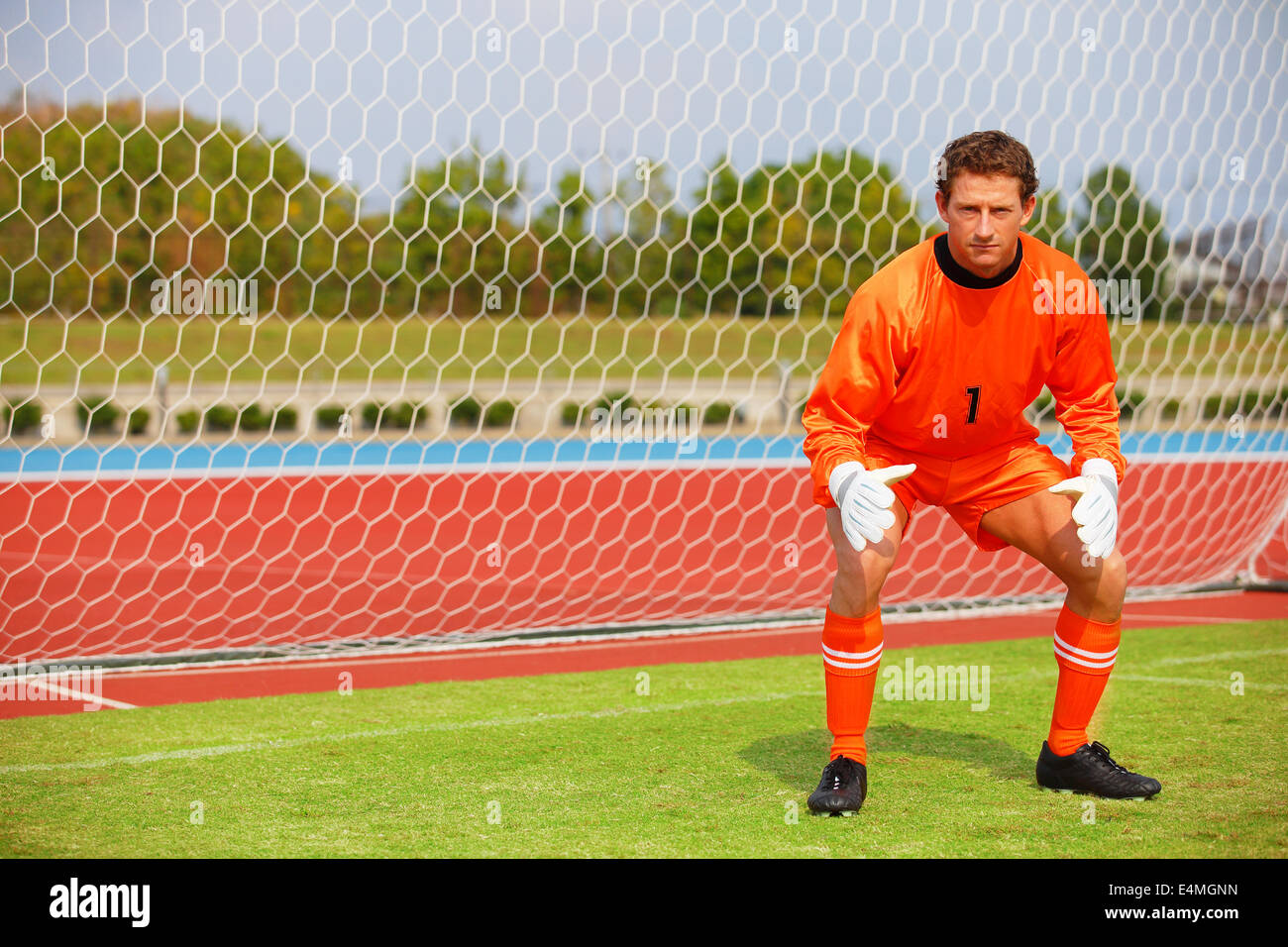 Goalkeeper in orange uniform standing in soccer field Stock Photo