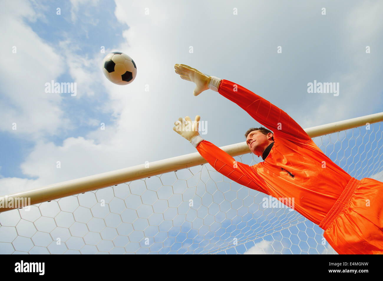 Goalkeeper in orange uniform catching the ball Stock Photo