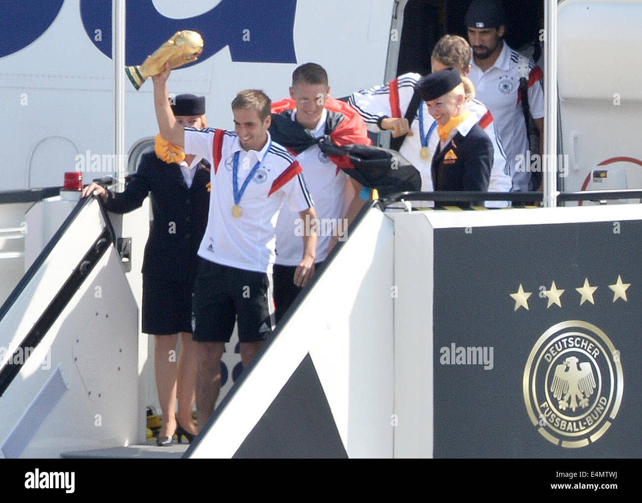 Berlin, Germany. 15th July, 2014. Germany's Philipp Lahm ( C), followed by his teammates Bastian Schweinsteiger and Thomas Mueller (R), step out of the aircraft holding the World Cup trophy in his hands as Germany's national soccer squad arrives at Tegel airport in Berlin, Germany, 15 July 2014. Team Germany won the Brazil 2014 FIFA Soccer World Cup final against Argentina by 1-0, winning the World Champion title for the fourth time after the 1954, 1974 and 1990 World Cups. PHOTO: BERND VON JUTRCZENKA/dpa/Alamy Live News Stock Photo