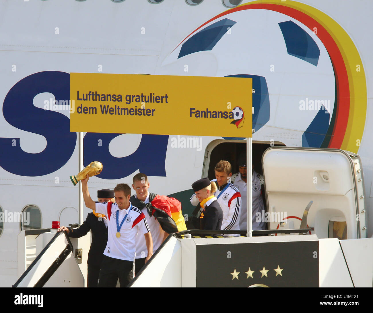 Berlin, Germany. 15th July, 2014. Germany's Philipp Lahm ( C), followed by his teammates Bastian Schweinsteiger and Thomas Mueller (R), step out of the aircraft holding the World Cup trophy in his hands as Germany's national soccer squad arrives at Tegel airport in Berlin, Germany, 15 July 2014. Team Germany won the Brazil 2014 FIFA Soccer World Cup final against Argentina by 1-0, winning the World Champion title for the fourth time after the 1954, 1974 and 1990 World Cups. PHOTO: JENS BUETTNER/dpa/Alamy Live News Stock Photo