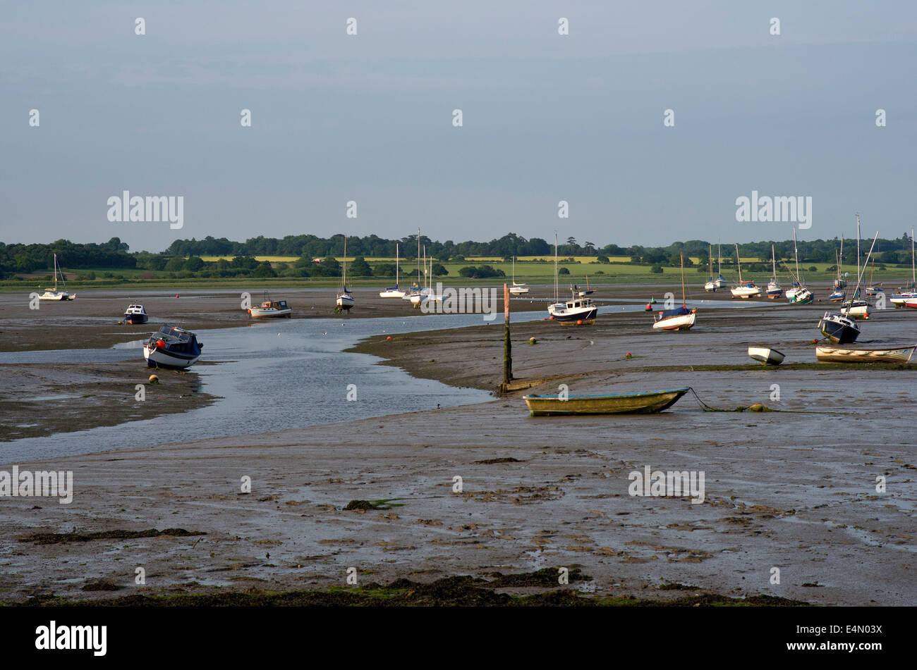 small boats resting on the mud of The River Stour aat low tide. The far shore is Suffolk Stock Photo