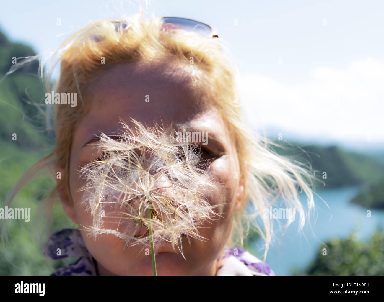 A blond woman blowing on a dandelion to make a wish Stock Photo