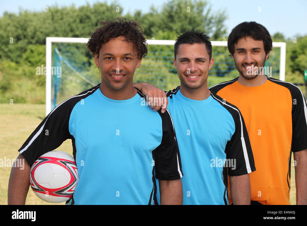 Three smiling footballers in front of goal Stock Photo