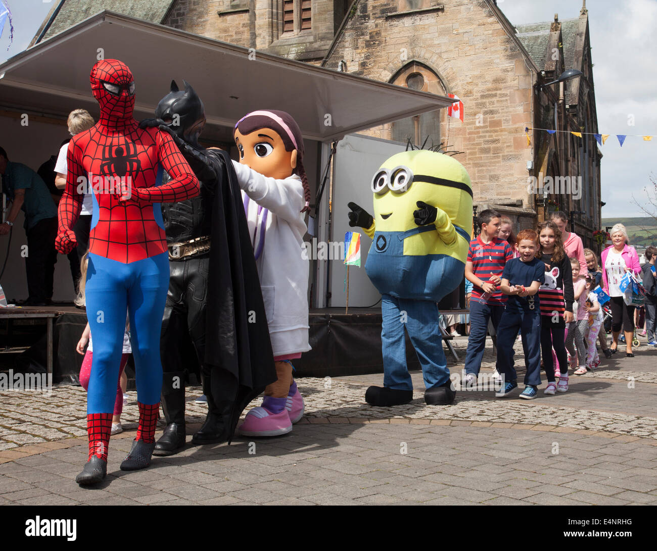 Ayrshire, Scotland, UK. 15th July, 2014. Spiderman and Batman lead a conga dance while waiting for the Queen's Baton Relay for the Glasgow2014 Commonwealth Games passes through the town of Dalry in North Ayrshire, Scotland. Stock Photo