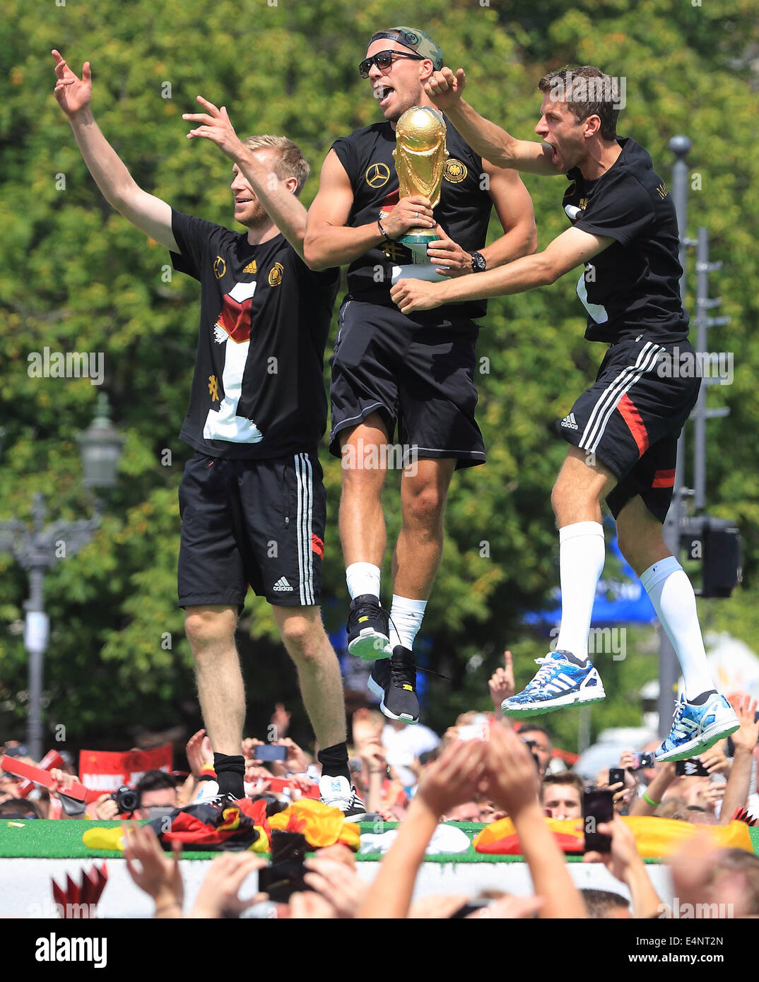 Berlin, Germany. 15th July, 2014. Germany's Per Mertesacker (L-R), Lukas Podolski, holding the World Cup trophy in his hands, and Thomas Mueller cheer and celebrate on stage during the welcome reception for Germany's national soccer team in front of the Brandenburg Gate, Berlin, Germany, 15 July 2014. The German team won the Brazil 2014 FIFA Soccer World Cup final against Argentina by 1-0 on 13 July 2014, winning the world cup title for the fourth time after 1954, 1974 and 1990. Photo: Jens Wolf/dpa/Alamy Live News Stock Photo