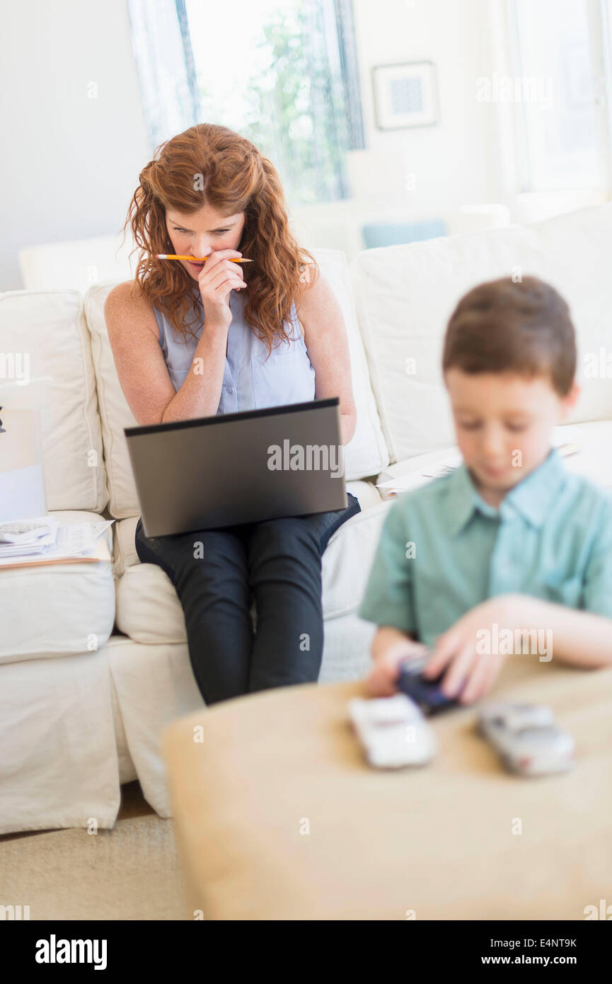 Mother using laptop, son (6-7) playing with toy cars Stock Photo