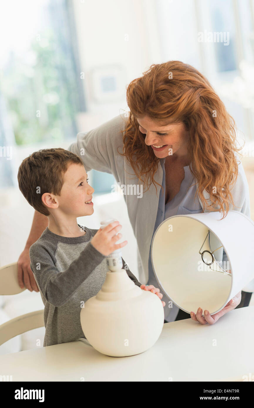 Son (6-7) and mother changing lightbulb in table lamp Stock Photo