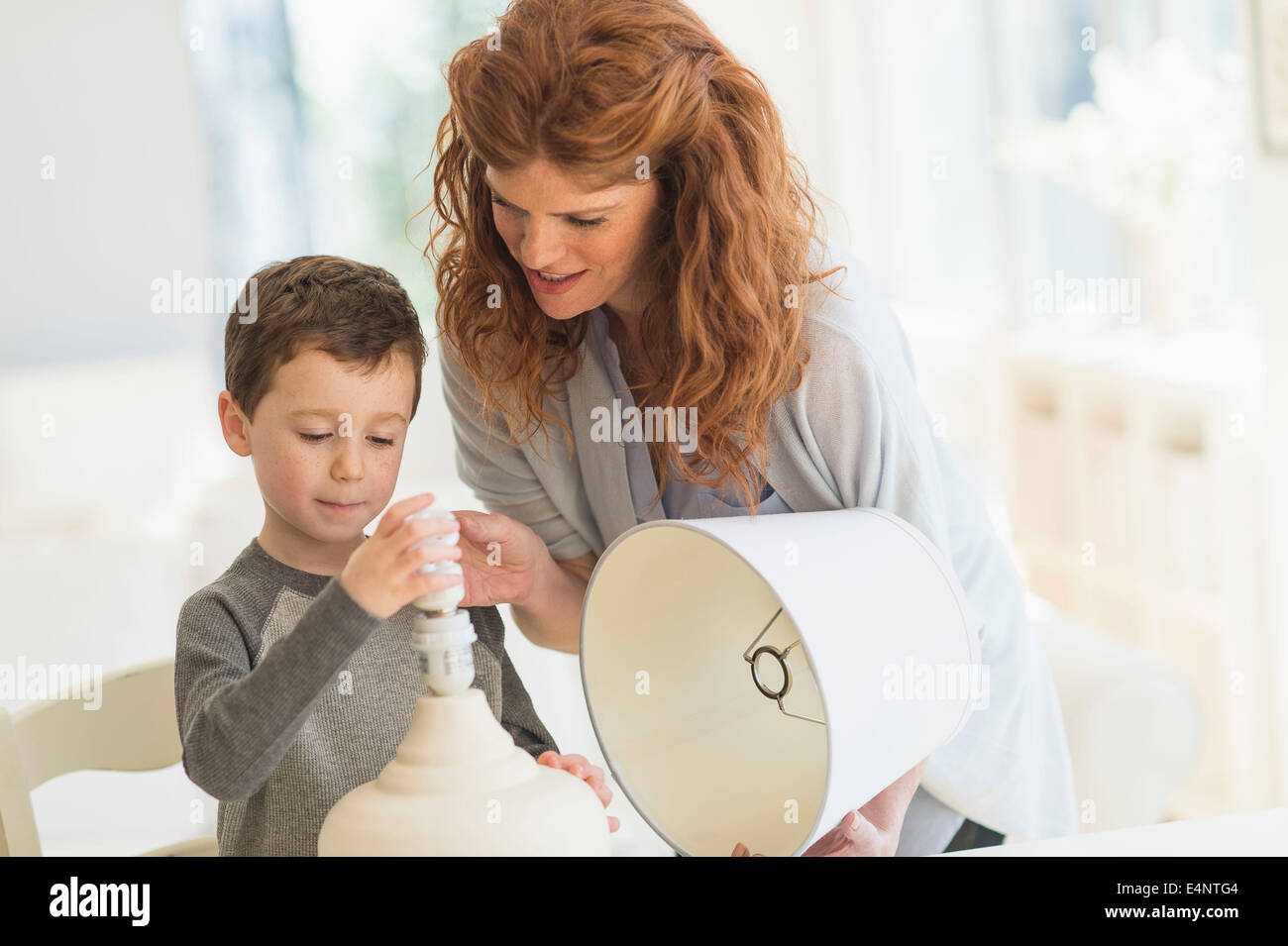 Son (6-7) and mother changing lightbulb in table lamp Stock Photo