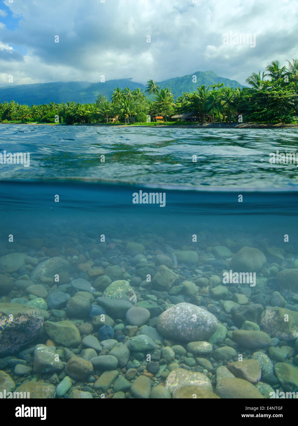beach in Bali, split shot with visible stones under water. North Bali with volcano mountains in background Stock Photo