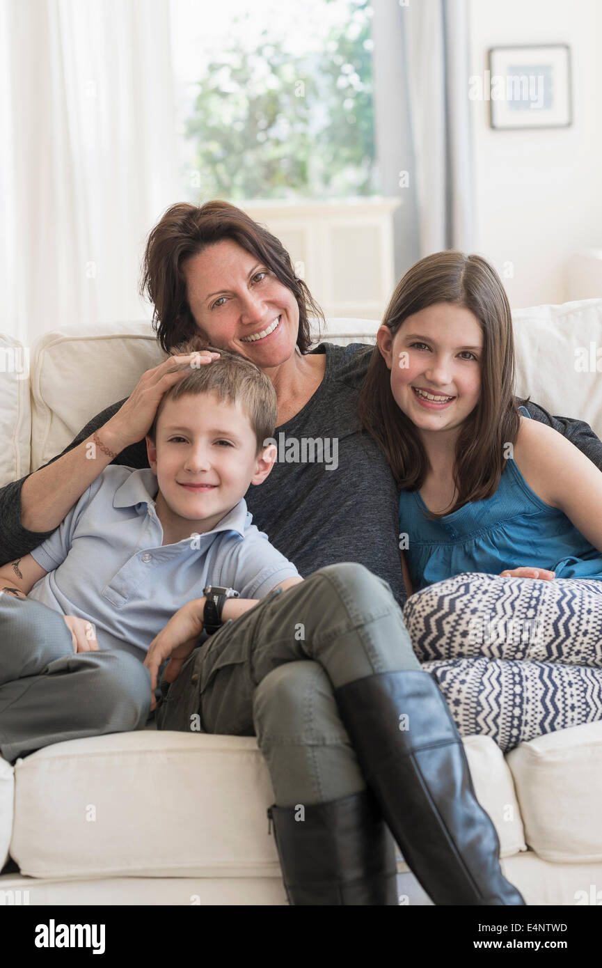 Mother and kids (8-9, 10-11) sitting on sofa Stock Photo