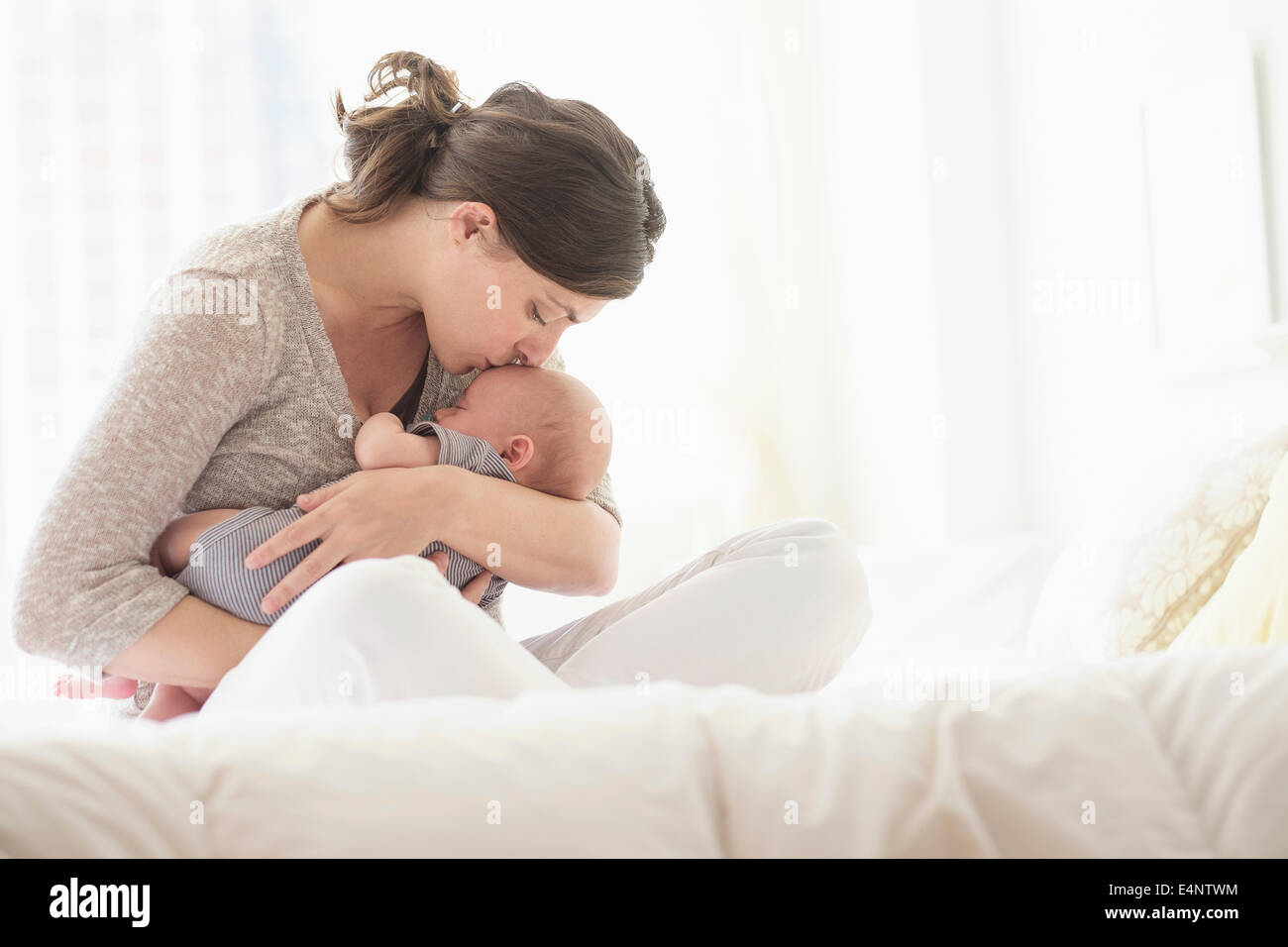 Mother kissing baby boy (2-5 months) in bed Stock Photo