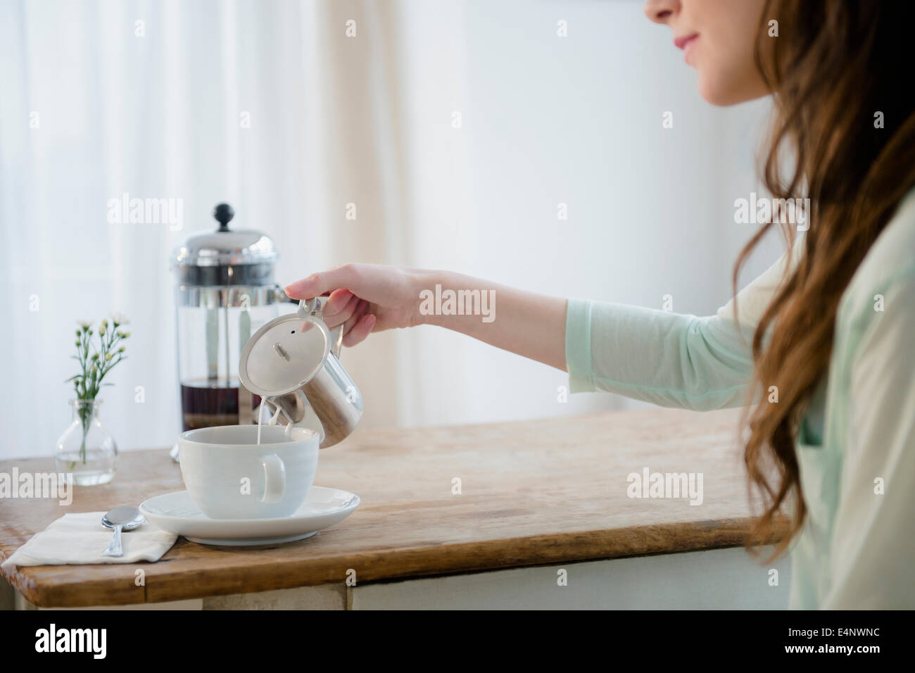 Young woman pouring milk into coffee cup Stock Photo