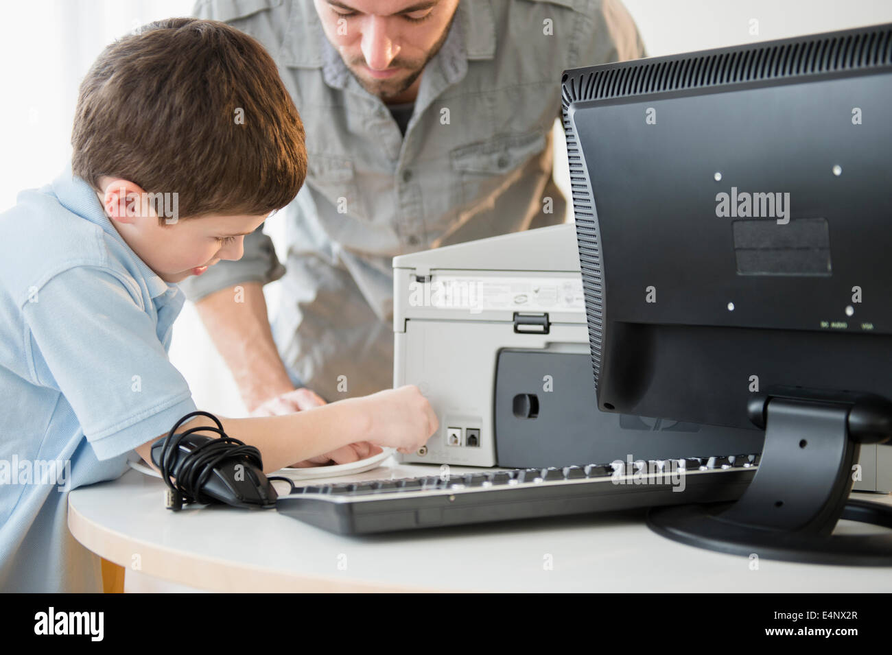 Father and son (8-9) setting up printer with computer on table Stock Photo